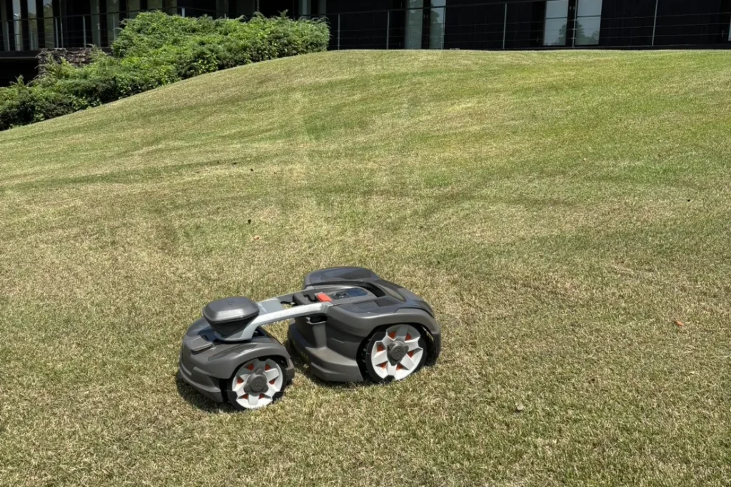 35度の傾斜地で芝を刈るAotomower435Xロボット芝刈り機。背景にはモダンな建物。