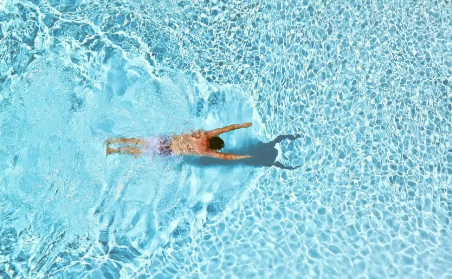 「クリアブルーのプールで泳ぐ人物の上空からのショット」
