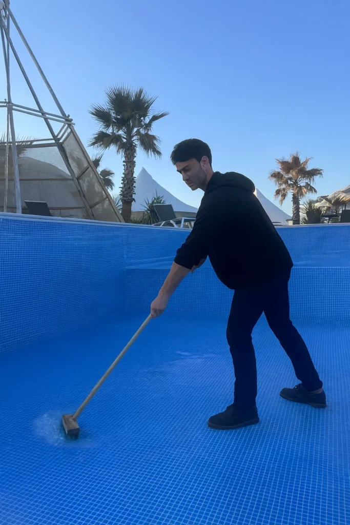 男性が屋外リゾート施設で空のプールを清掃している様子