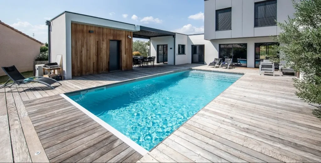 木製デッキに囲まれたマジラインプールとモダン住宅。屋外ダイニングとサンラウンジャーが並ぶ上質なプール空間